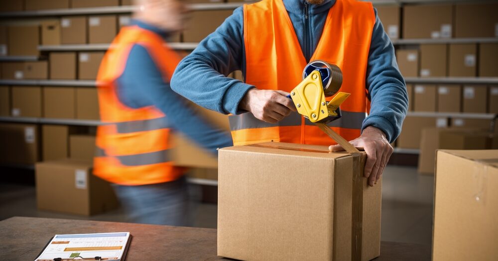 Warehouse,Worker,Sealing,A,Delivery,Box,Using,A,Tape,Dispenser