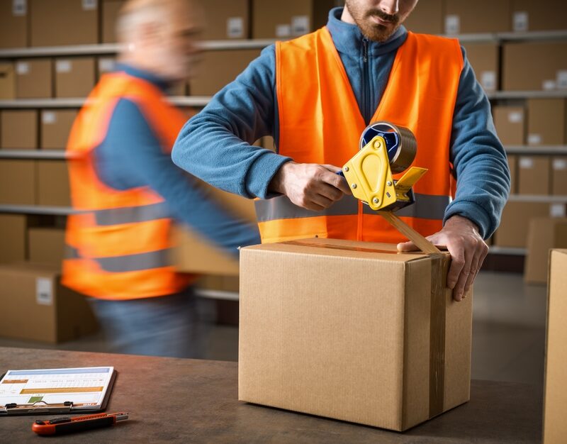 Warehouse,Worker,Sealing,A,Delivery,Box,Using,A,Tape,Dispenser